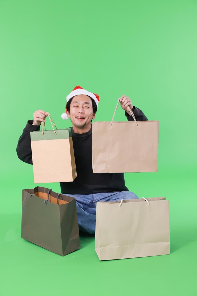 「クリスマスセールで買い物しまくる男性（グリーン背景）」の写真［モデル：大川竜弥］