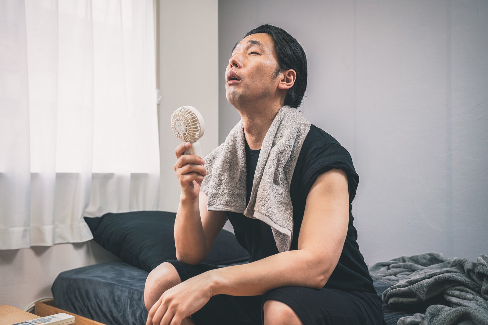 「携帯扇風機の風で暑さをやり過ごす男性」の写真［モデル：大川竜弥］