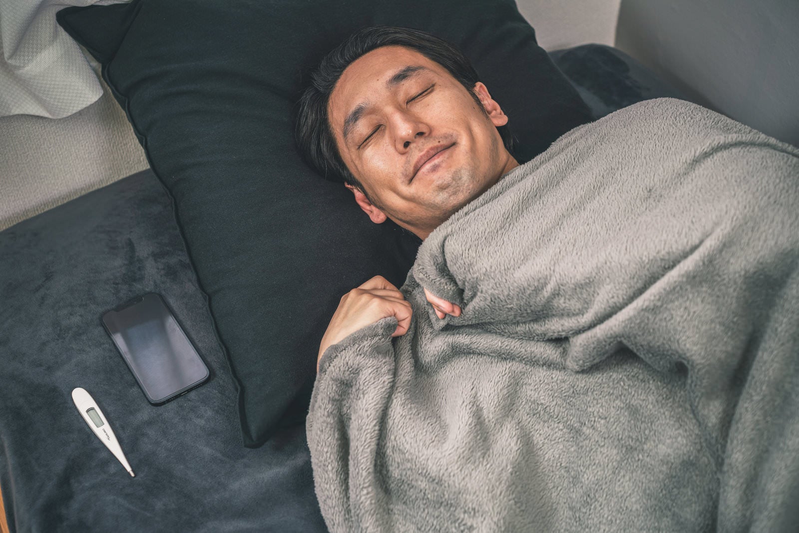 「枕元にスマホと体温計を置いて就寝する男性」の写真［モデル：大川竜弥］