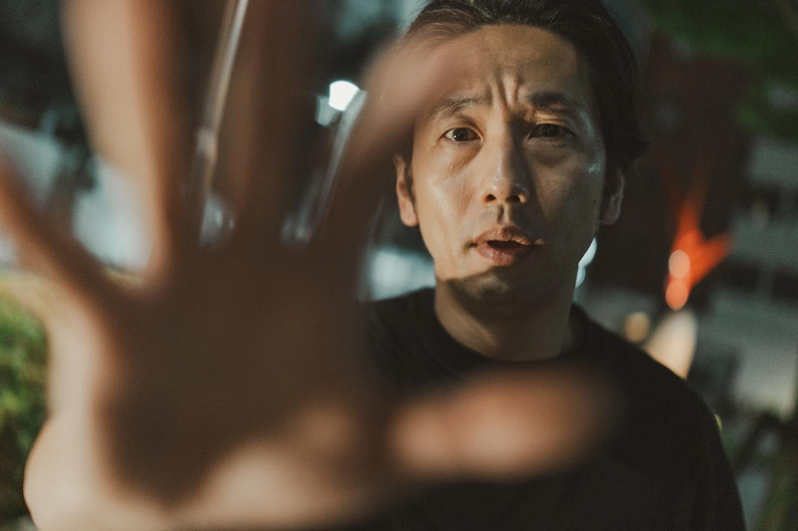 夜間の屋外でマイクを向けられながら身体への接触を拒否する困惑した男性［モデル：大川竜弥］