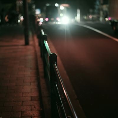 夜のガードレールと車のハイビームの写真