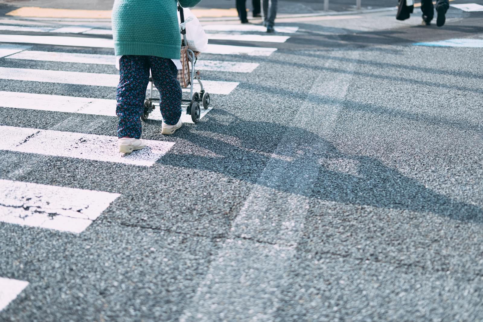 「手押し車を押して横断歩道を渡る女性」の写真