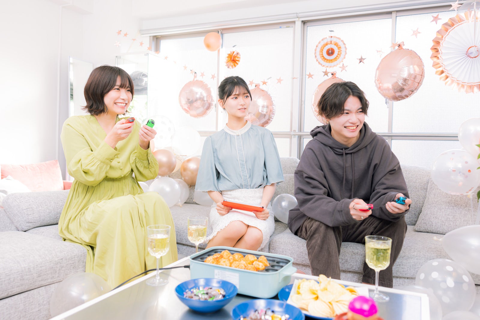 「ホームパーティで家庭用ゲームをプレイする男女三人」の写真［モデル：SHUN モデルリリース 夏実］