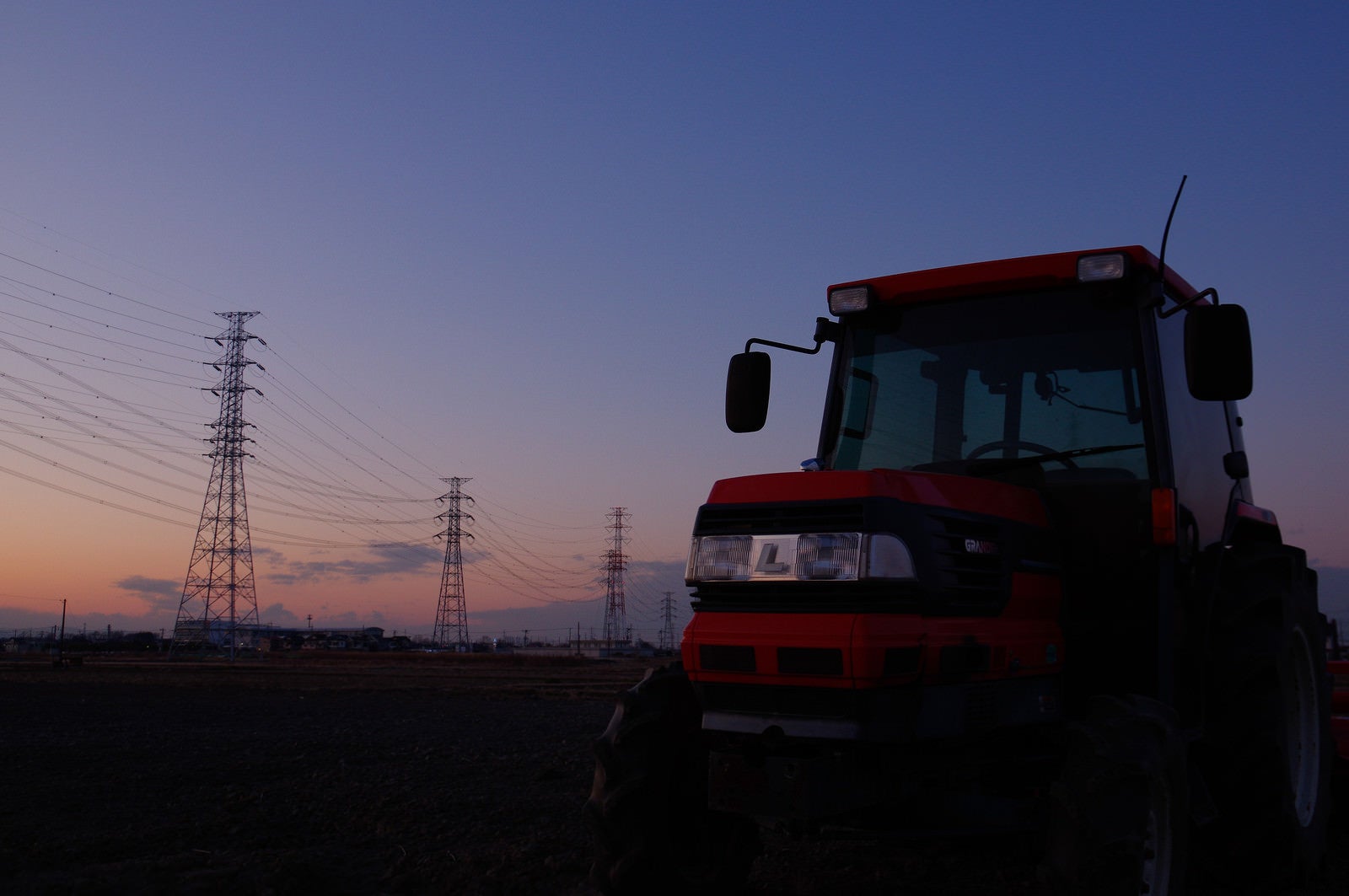「夕暮れ時の送電線とトラクター」の写真