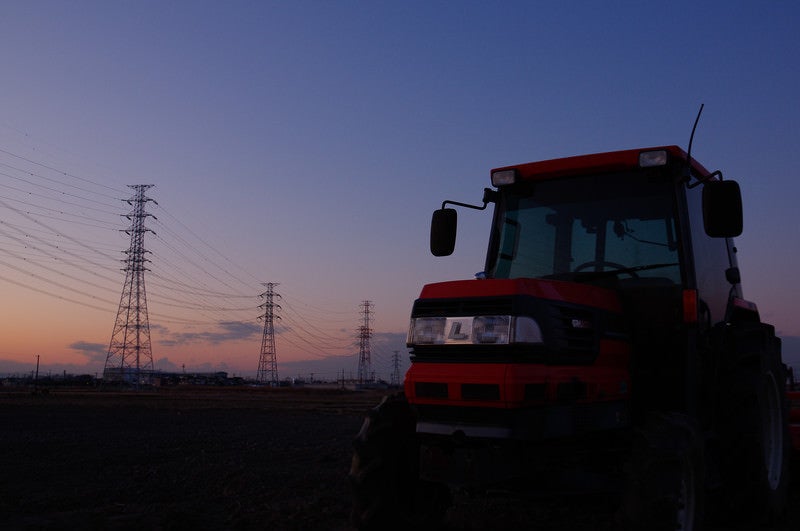 夕暮れ時の送電線とトラクターの写真