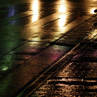 雨に濡れた道路と反射するヘッドライトの写真