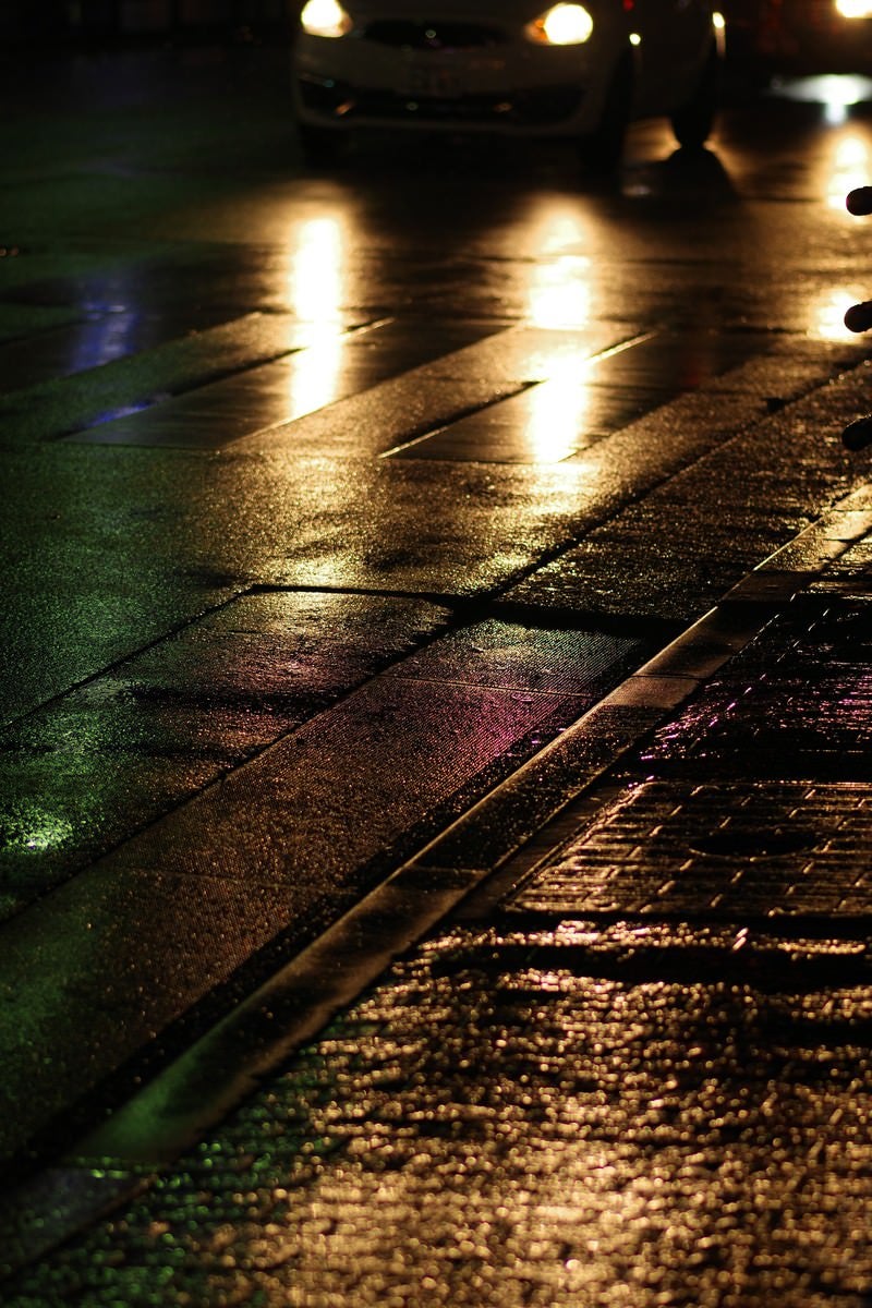 「雨に濡れた道路と反射するヘッドライト」の写真