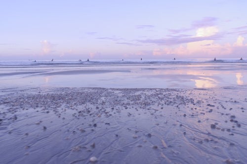 早朝から海に出るサーファーの写真