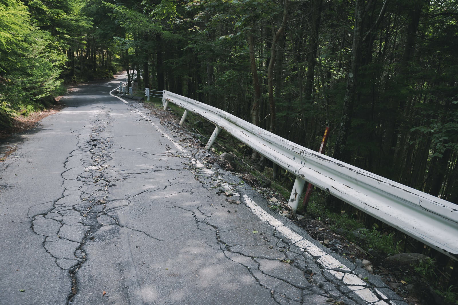 「ひび割れた道路と傾いたガードレール」の写真