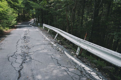 ひび割れた道路と傾いたガードレールの写真