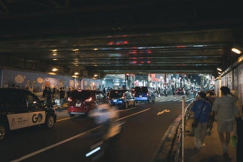 新大久保駅高架下の歩行者と信号待ちの車（夜間）の写真
