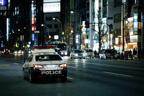 夜の繁華街を巡回するパトカーの写真