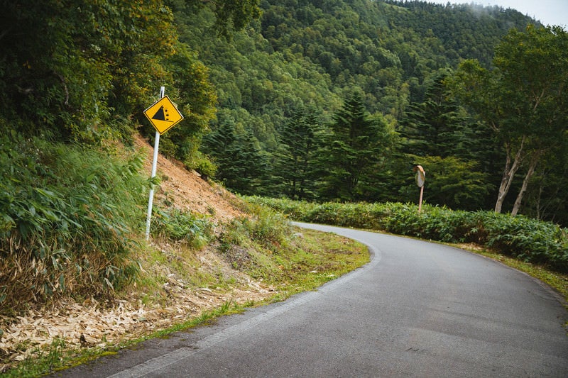 落石注意の看板と峠道の写真