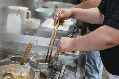 麺が固まらないようにテボに箸を入れる様子の写真