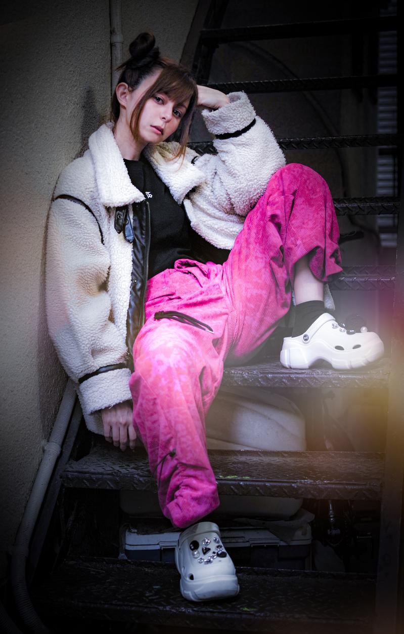 「アパートの階段でもたれかかるピンクパンツと白ジャケットの女性」の写真［モデル：ラミエル］