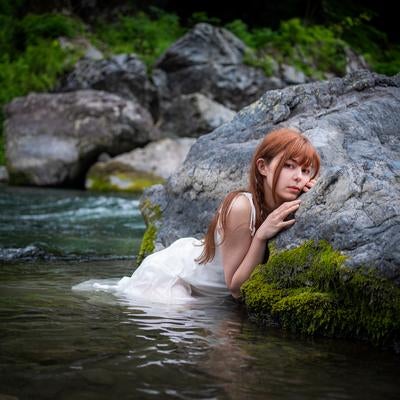 川の岩場で白いドレスに水を浴びる女性のポートレートの写真