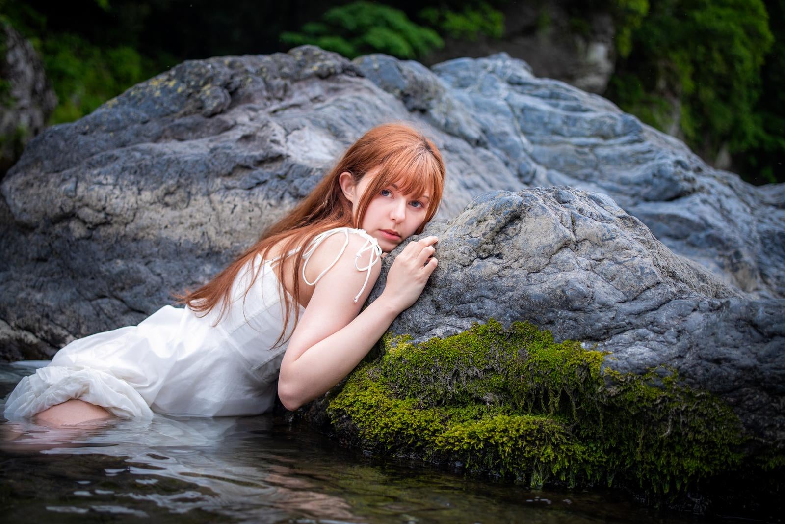 「川辺の岩に寄りかかる白いドレスの女性のポートレート」の写真［モデル：ラミエル］