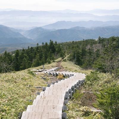 四阿山山頂へ導く木製遊歩道と霞む山並みの風景の写真