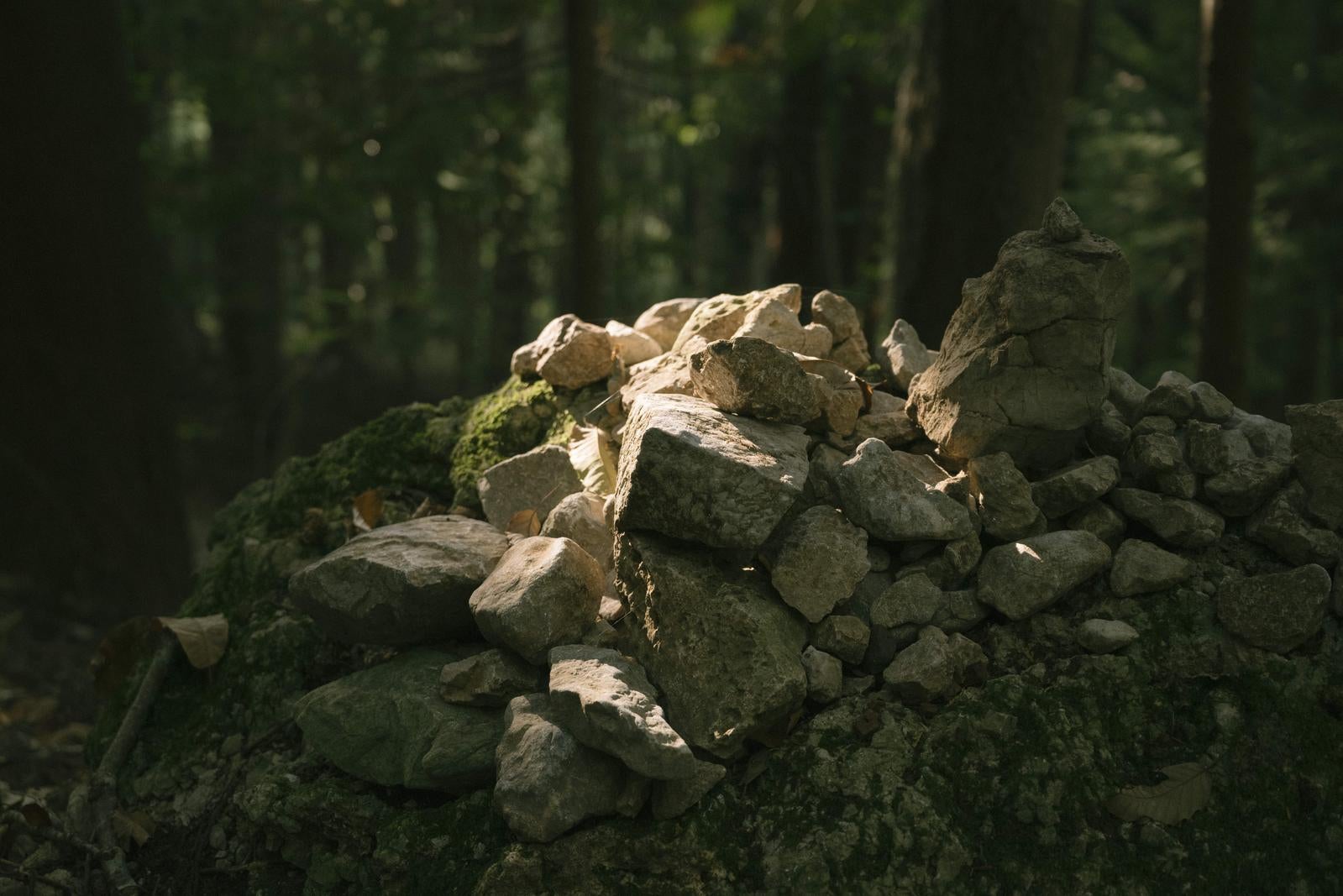 「苔むした岩の上に丁寧に積み上げられた光が差す積石」の写真