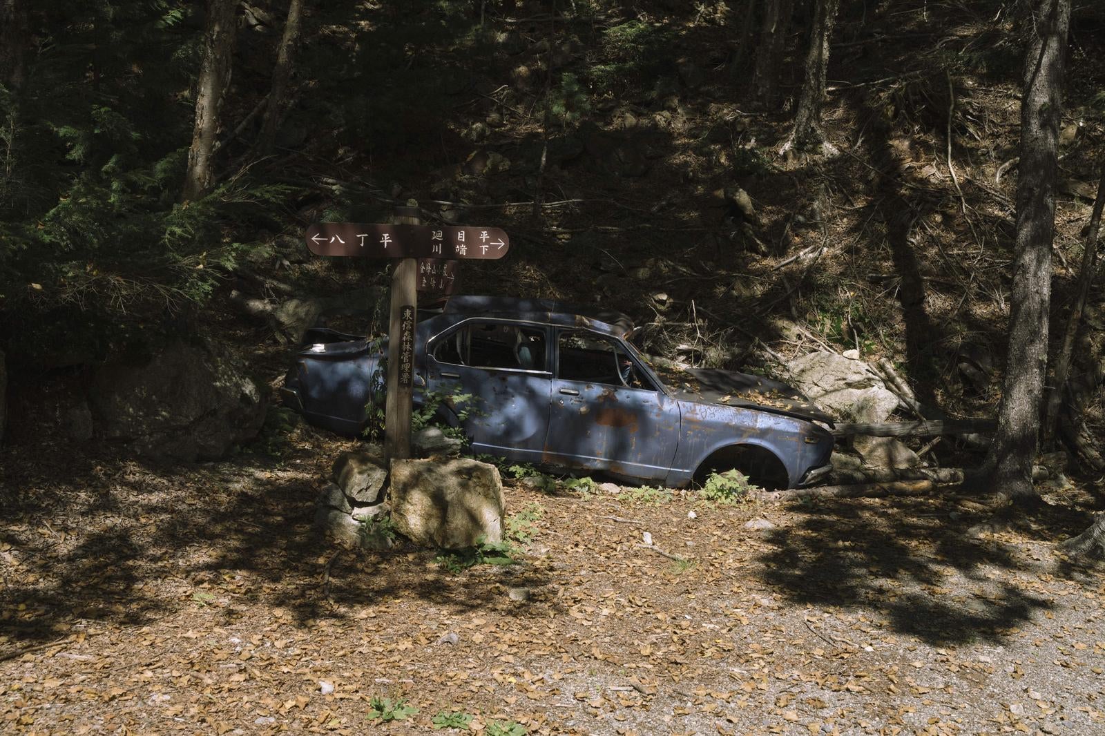 「朽ちた青い車と道標が並ぶ山中」の写真