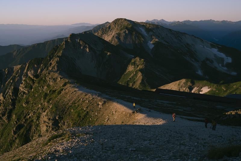 雄大な山脈を背景に歩むハイカーたちの姿の写真