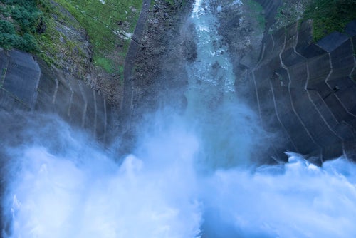 激しく放水を行う黒部ダムを上から見る（立山）の写真