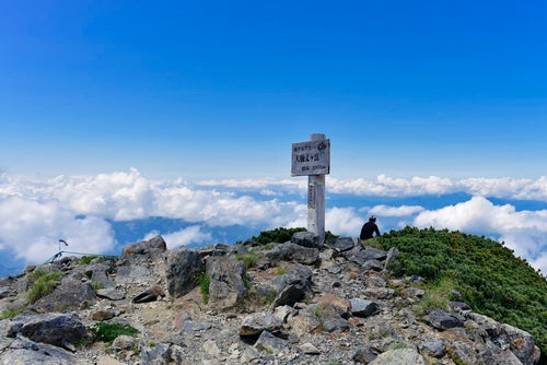 大仙丈岳山頂に佇む登山者と眼下の雲の写真