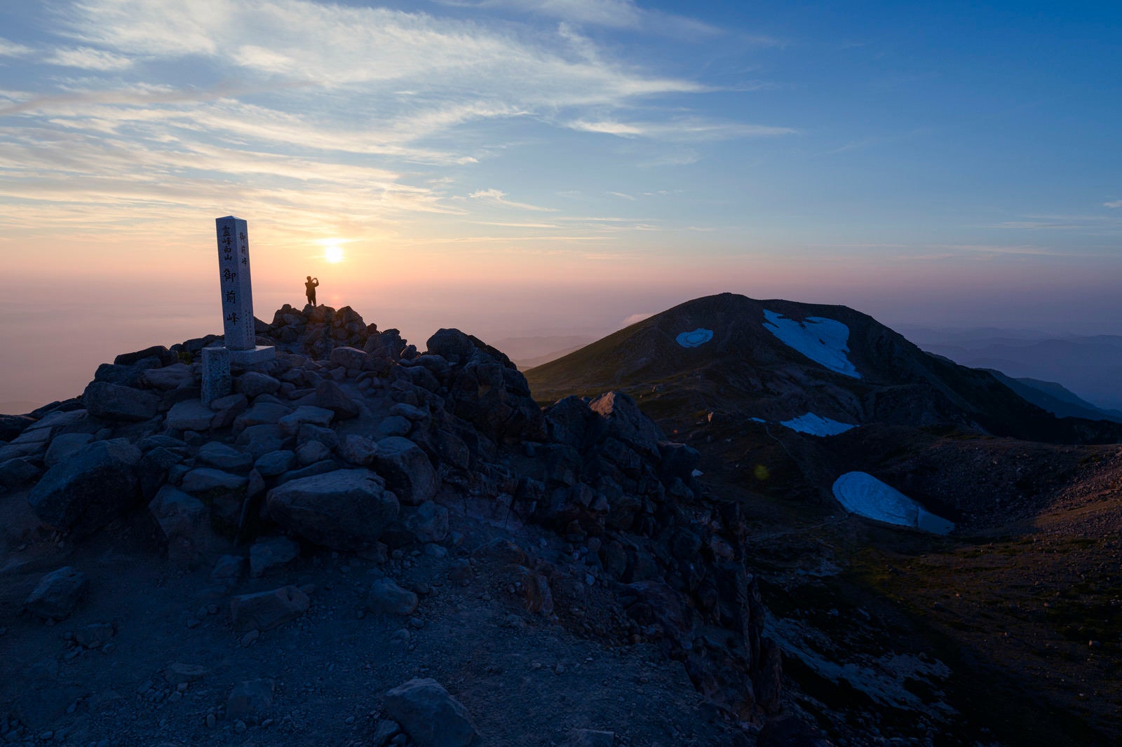「夕日を楽しむ登山者と御前峰山頂碑（白山）」の写真