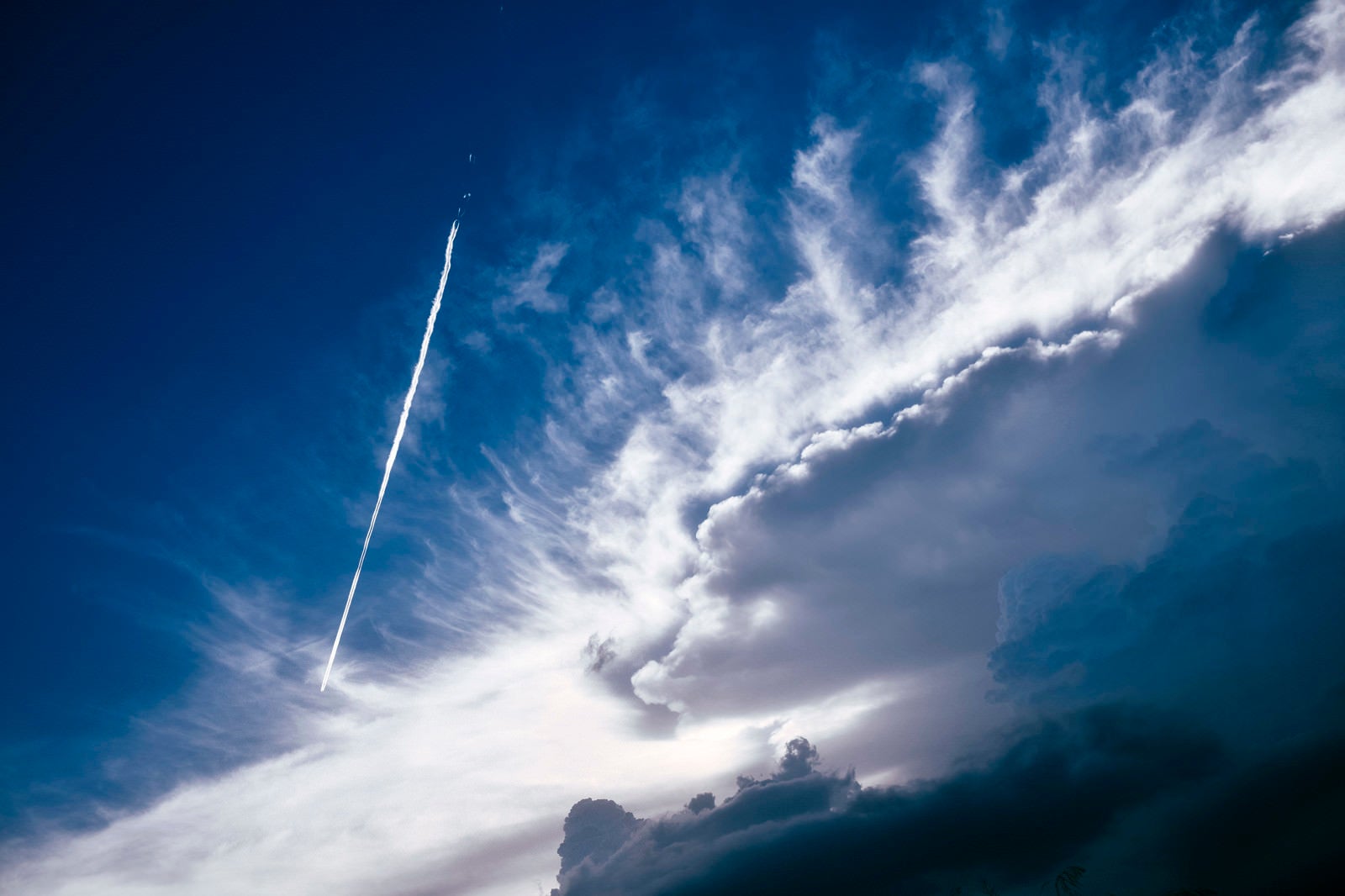 「かなとこ雲のそばを飛んで行く飛行機雲」の写真