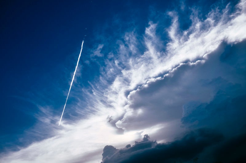 かなとこ雲のそばを飛んで行く飛行機雲の写真