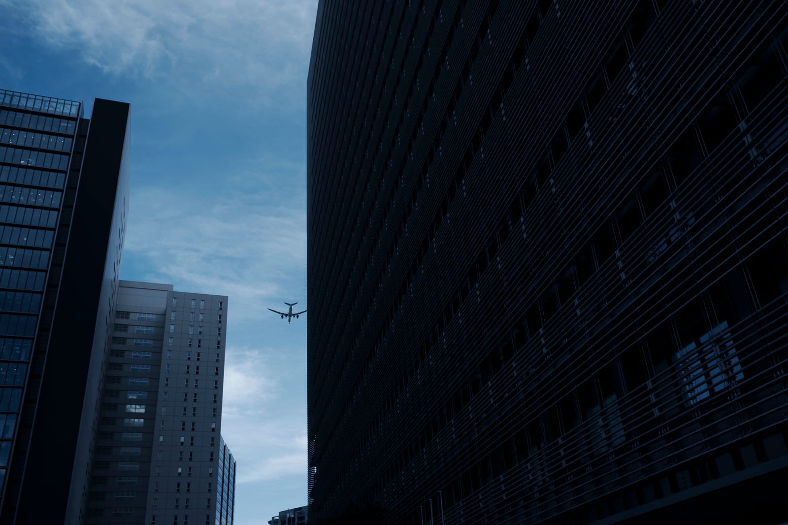 「ビルの隙間の向こうへと跳んで行く飛行機」の写真