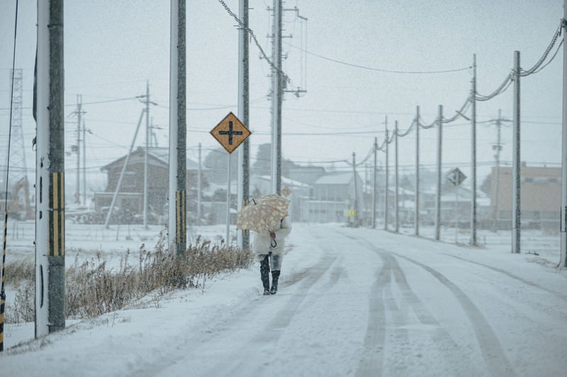 雪に残るタイヤ跡と降雪と吹雪の中を歩く歩行者の写真