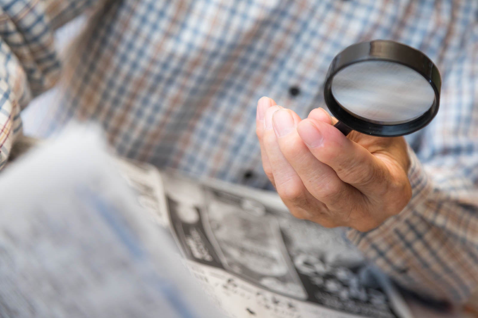 「手持ち拡大鏡で新聞を読む高齢者の手」の写真［モデル：まーちゃん］