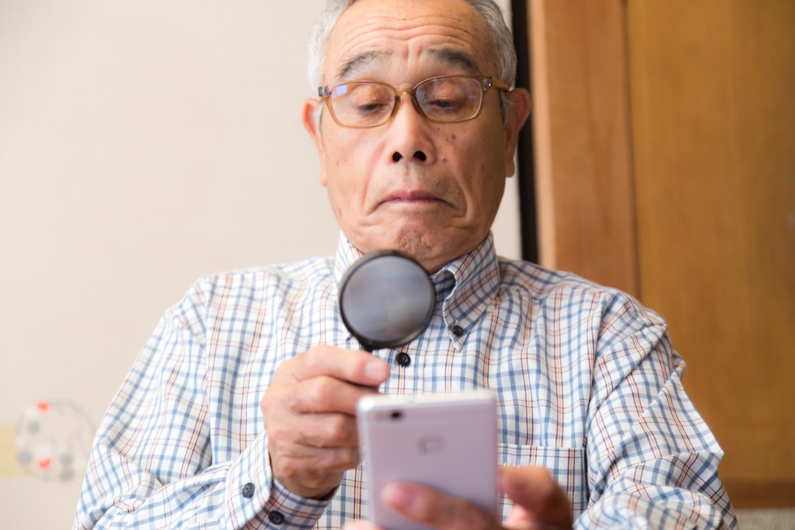「携帯の画面が小さくて拡大鏡を使うおじいさん」の写真［モデル：まーちゃん］