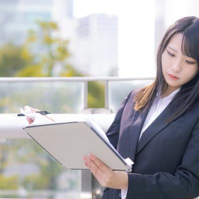 ビジネススーツを着た女性が屋外で書類を見ながら仕事をしている様子の写真