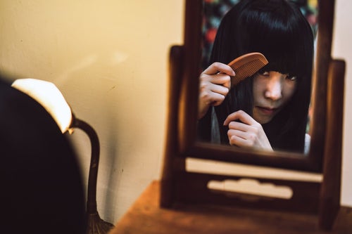 化粧台の小さな鏡で櫛を通す女性の写真
