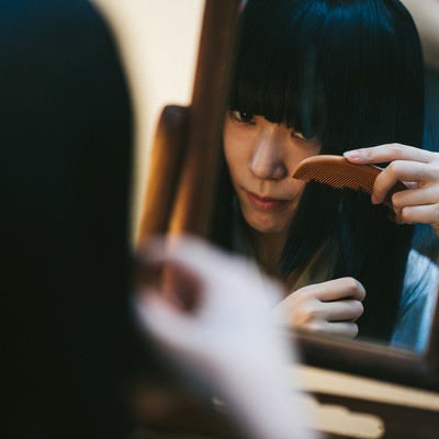 鏡を使って髪をとかす日本女性の写真