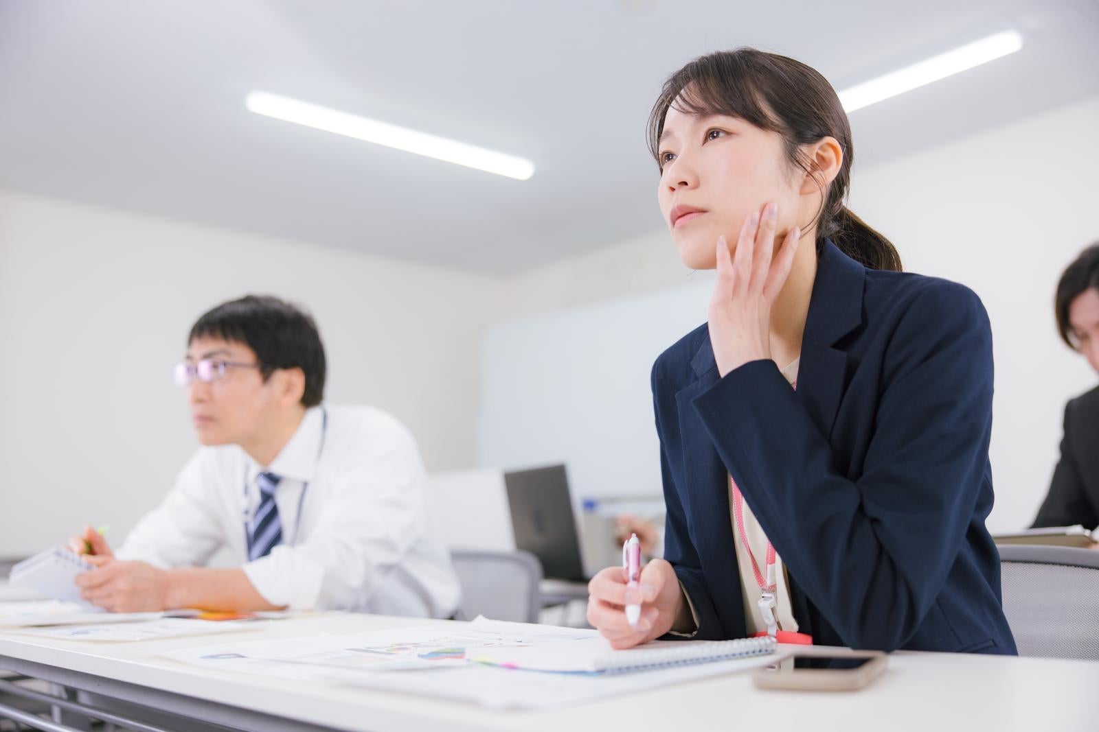 「オフィス会議で資料を確認しながら頬杖をつくビジネスウーマン」の写真［モデル：SAKI］