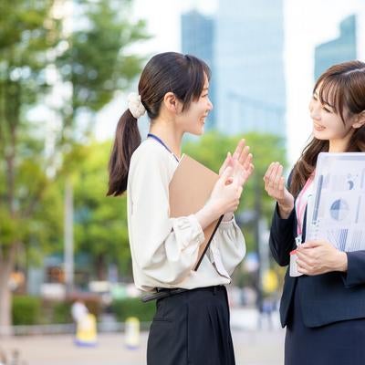 資料をもって立ち話をする女性社員ふたりの写真