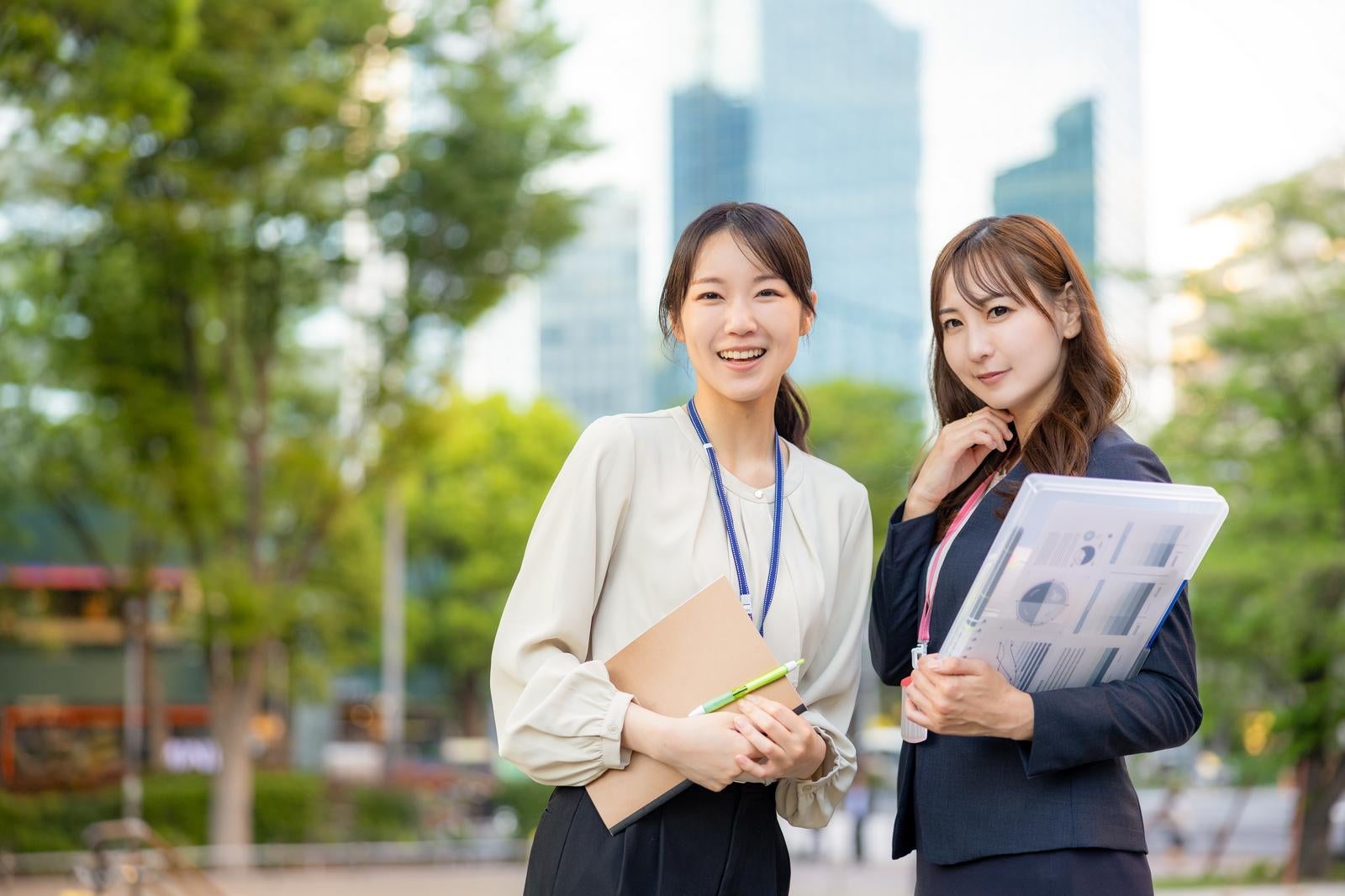 「高層ビルを背景にポーズを取るビジネスウーマンふたり」の写真［モデル：SAKI あゆみん］