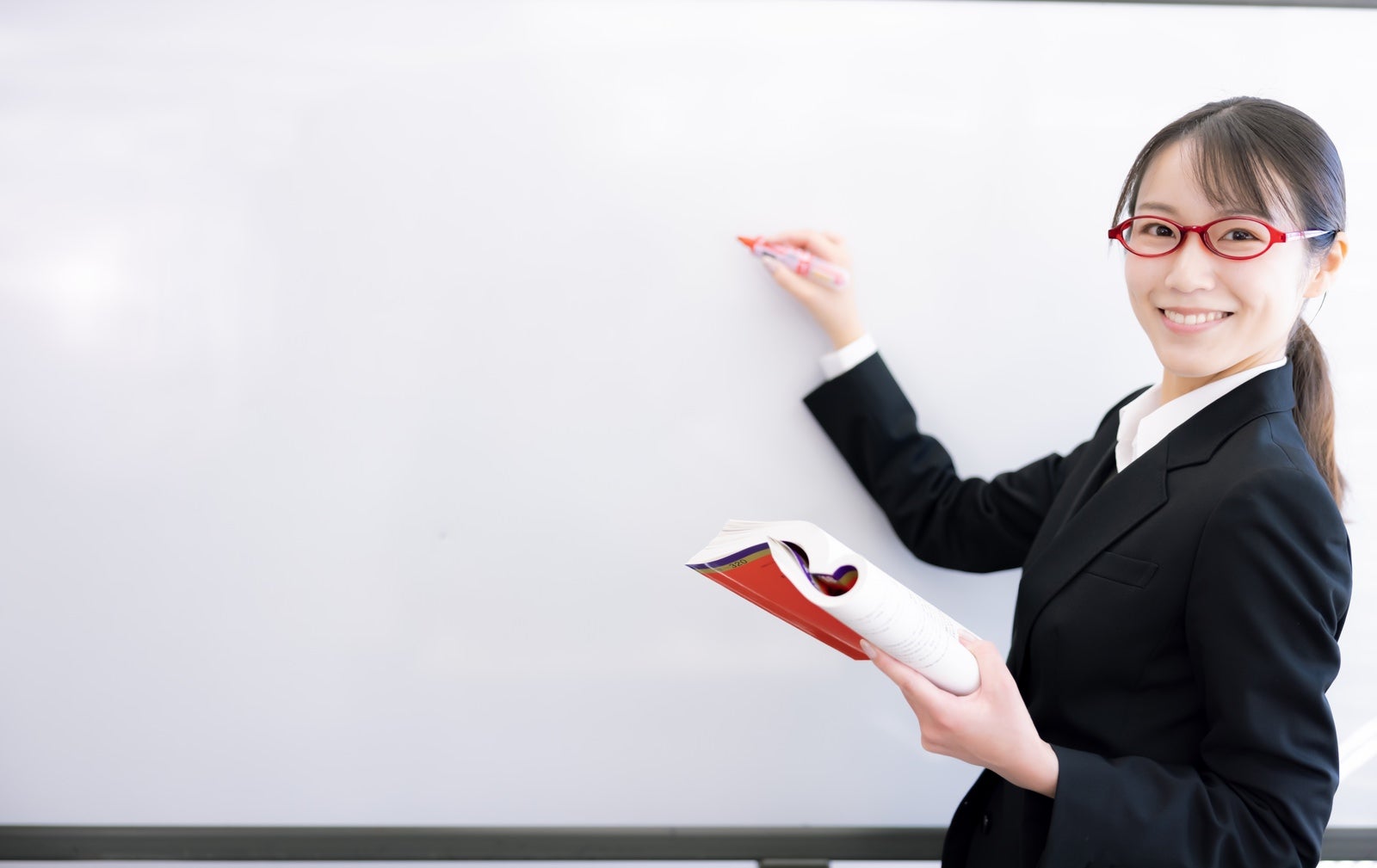 「笑顔で解答する赤い眼鏡の女性講師」の写真［モデル：SAKI］