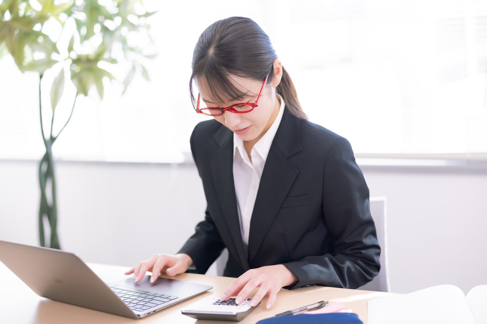 「電卓とノートパソコンを使いこなす女性社員」の写真［モデル：SAKI］