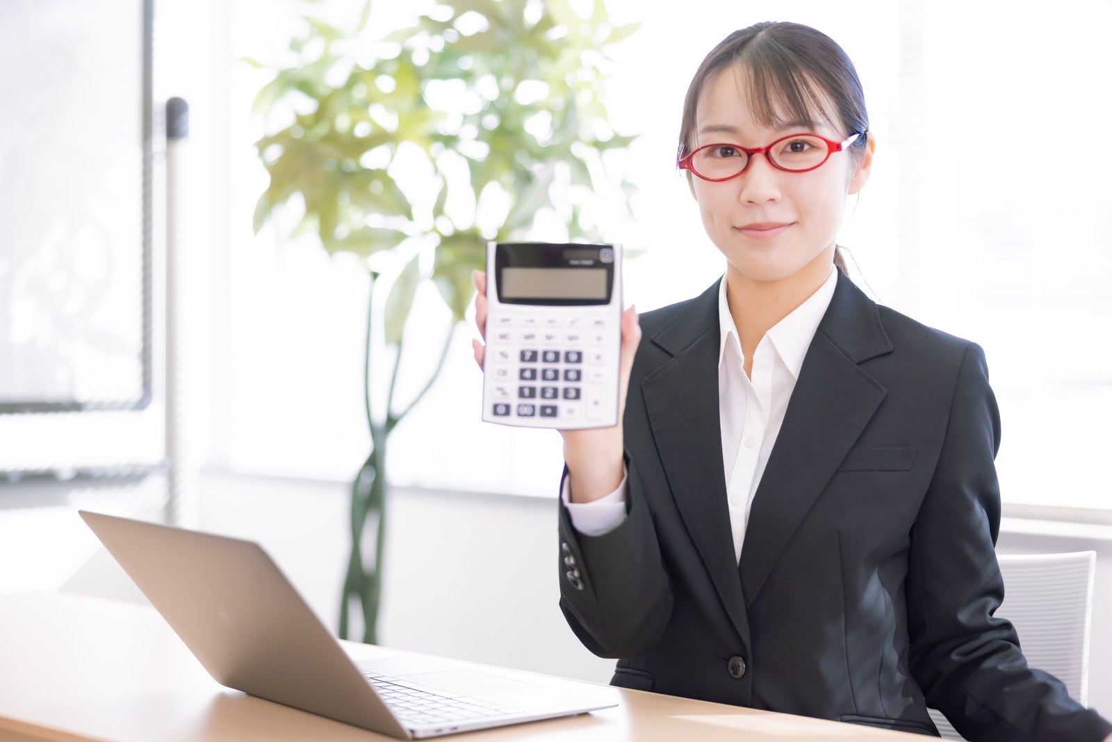「電卓をこちらに向ける女性会社員」の写真［モデル：SAKI］