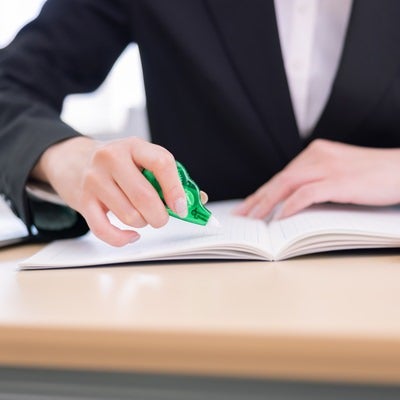 緑色の修正テープで書類を訂正する女性の手元の写真