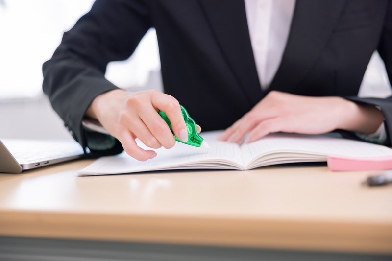 緑色の修正テープで書類を訂正する女性の手元の写真