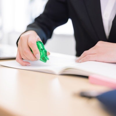 オフィスの机上で書類に修正テープを当てて訂正作業をする女性の手元の写真