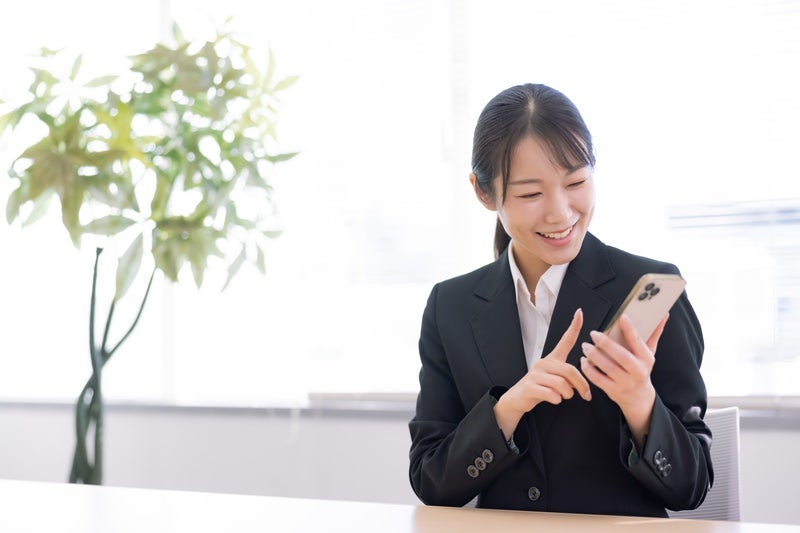 スマホを操作する笑顔のスーツ姿の女性