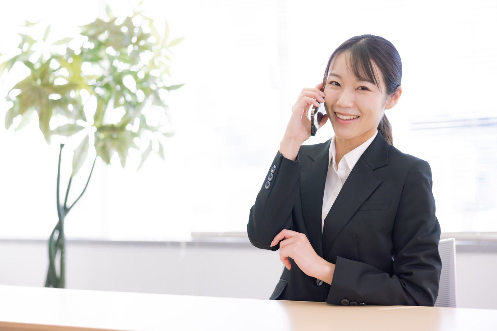 スマートフォンで通話中に微笑む黒いスーツを着た女性［モデル：SAKI］