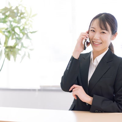 スマートフォンで通話しながら微笑む黒いスーツの女性の写真