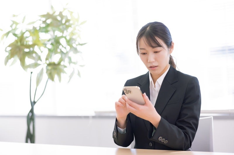 スマホを操作して困惑するスーツ姿の女性